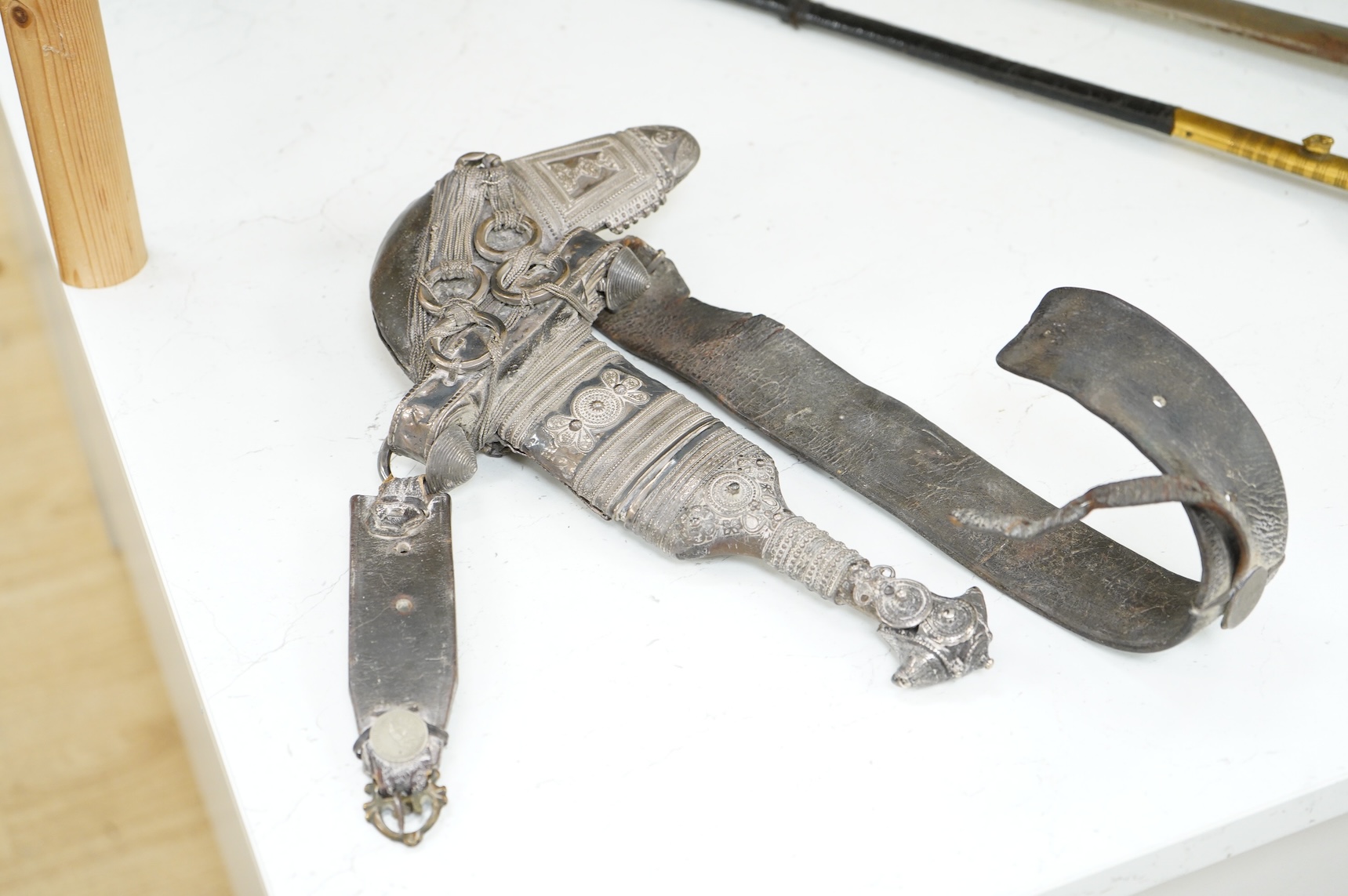 A late 19th century Arab silver mounted dagger jambya with silver filigree mounts to hilt and sheath, in its leather covered scabbard with parts of the original belt